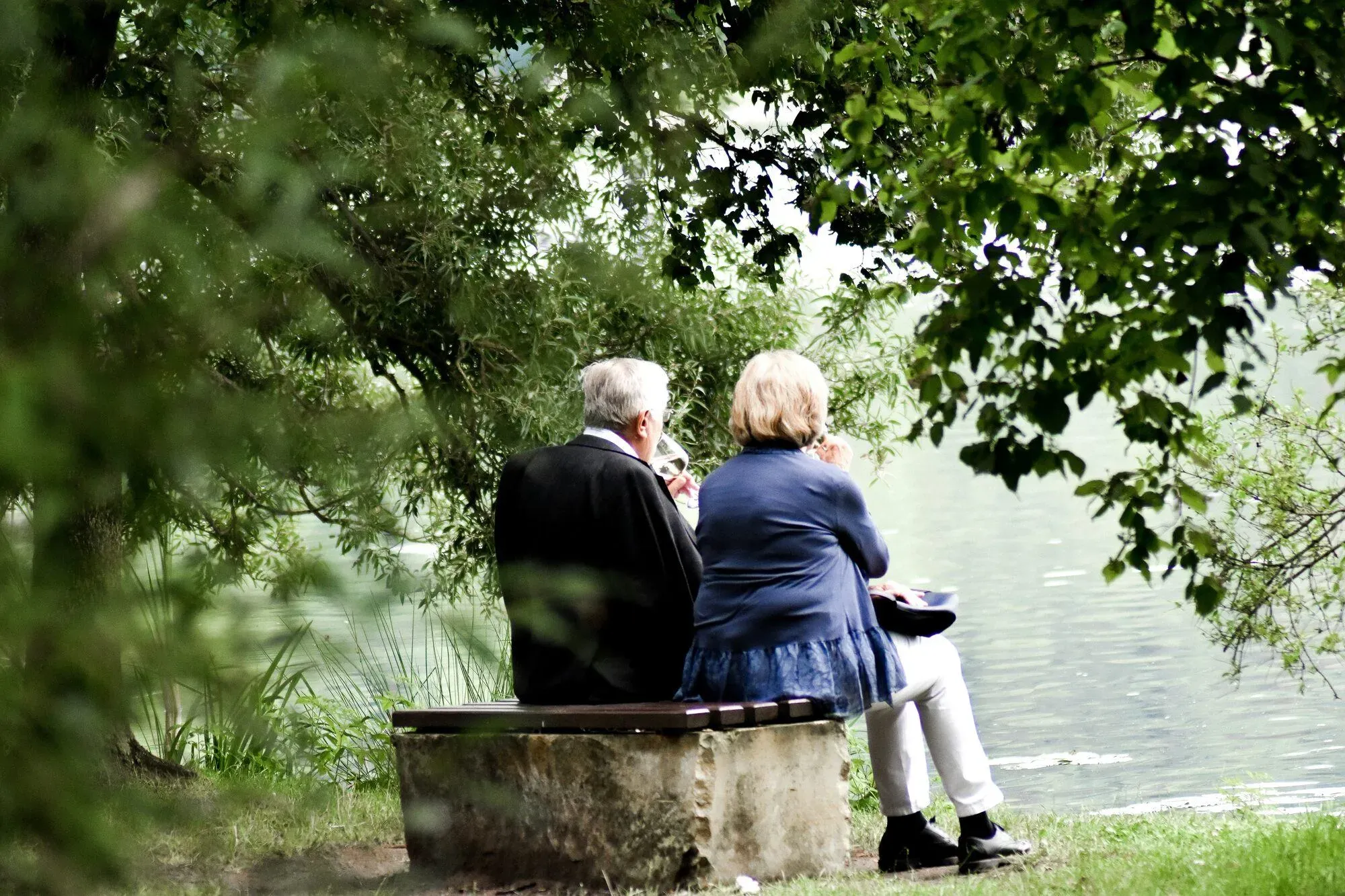Couple de retraités assis sur un banc à l'ombre des arbres au bord d'un lac