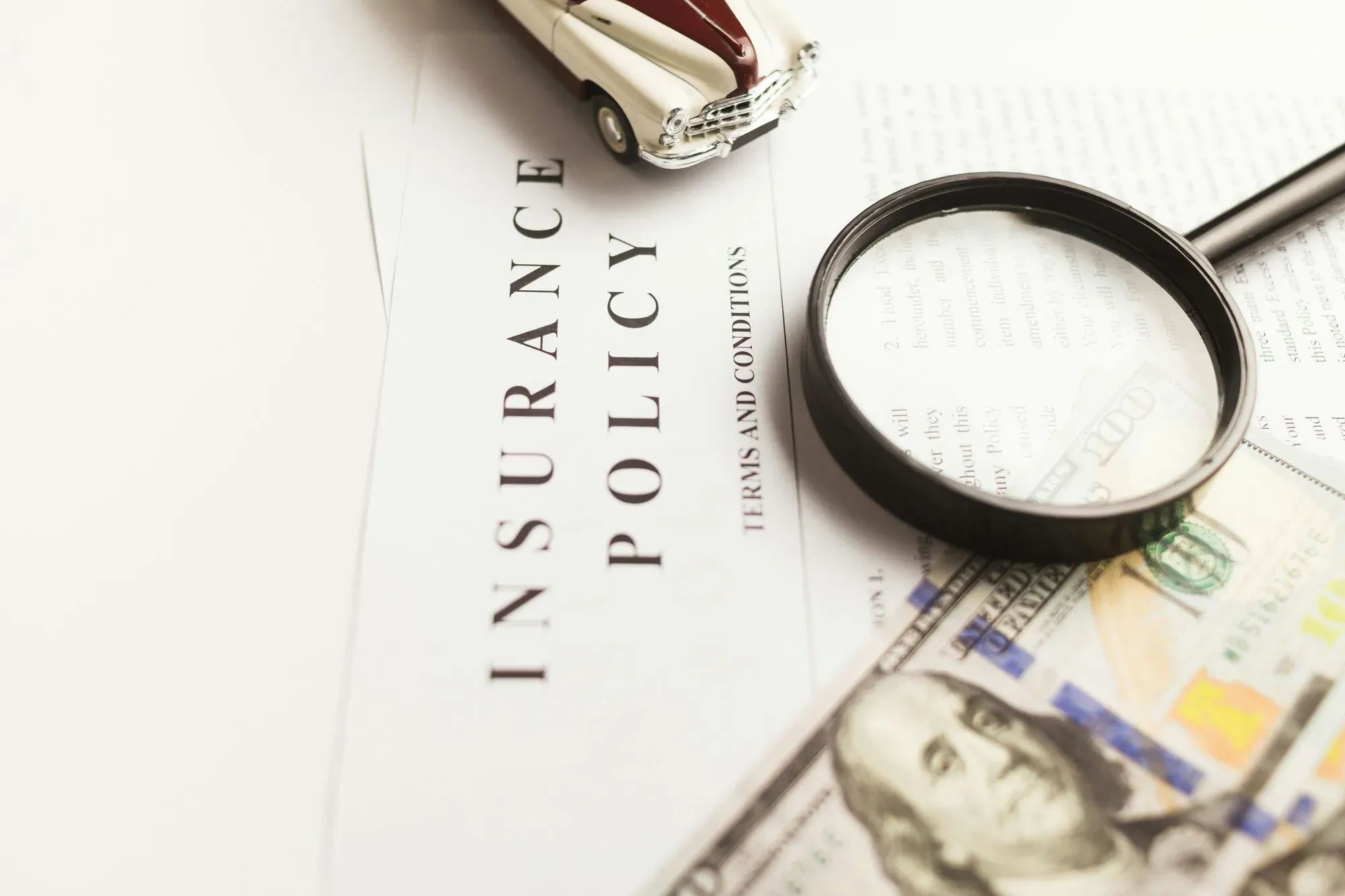 Document d'assurance examiné à la loupe, avec billets de dollars et voiture miniature