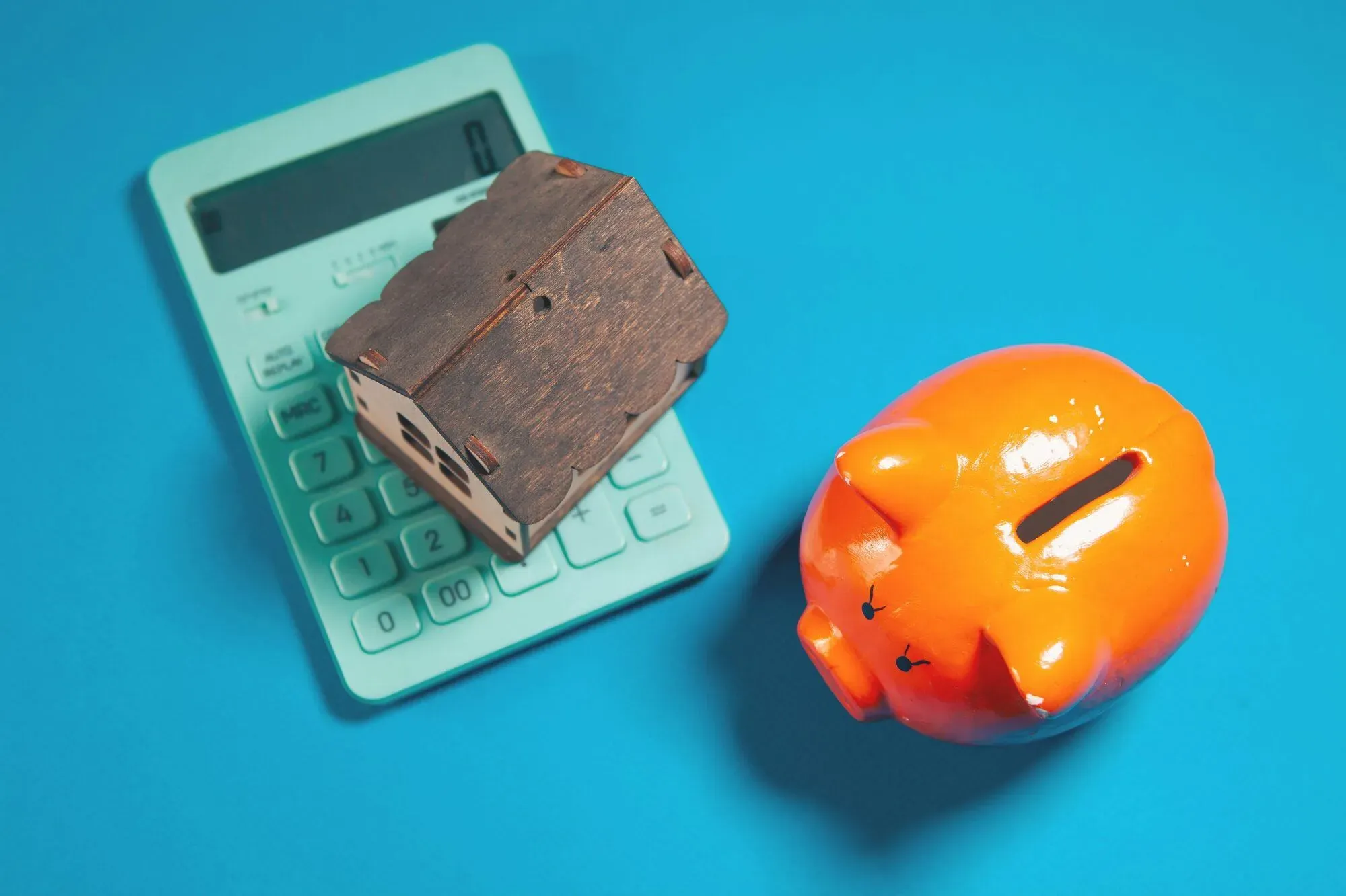 Maison miniature en bois posée sur une calculatrice à côté d'une tirelire cochon